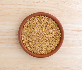 Bowl of organic golden flaxseed on a wood table top illuminated with natural light