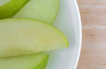 Green apple slices on a white plate atop a wood table top close view