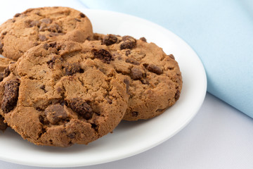 Side view of a plate of gourmet milk chocolate chip cookies with a blue napkin.