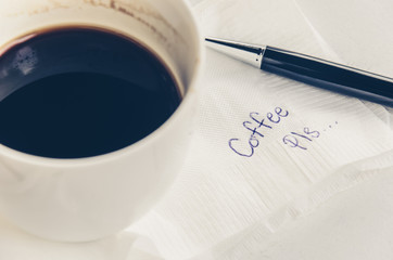 A cup of Coffee and pen with word and emoticon smiling face handwriting on a napkin with a cup of coffee