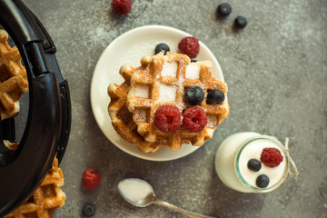 Homemade Belgian waffles with forest fruits, blueberries, raspberries over grey background. Vintage styling. Top view.