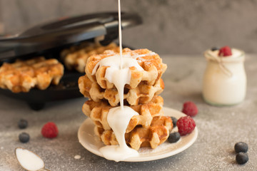 Homemade Belgian waffles with forest fruits, blueberries, raspberries and with shedding yogurt over grey background. Vintage styling. Toning.