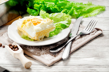 
breakfast or lunch , air , beaten egg and baked in the oven , with lettuce and herbs on a white wooden background