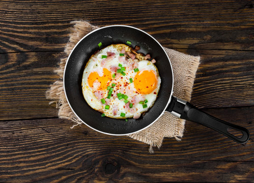 Fried eggs in pan on wooden background.