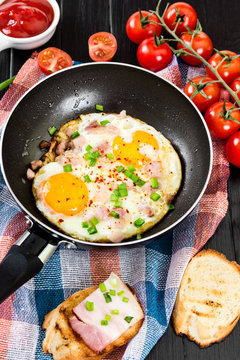 Fried eggs with onion in pan on black background.