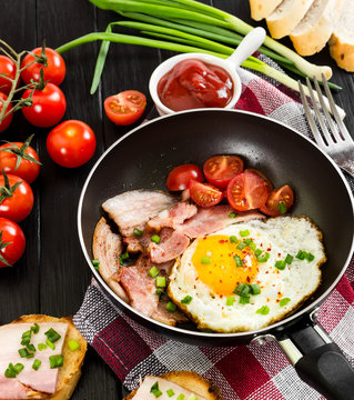 Fried eggs with ham in pan on black background.
