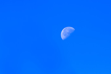 the white moon visible on a clear sky blue day