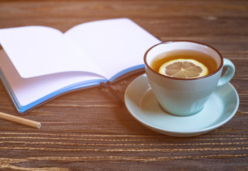 Hot tea with lemon and notebook on wood background - seasonal relax concept 