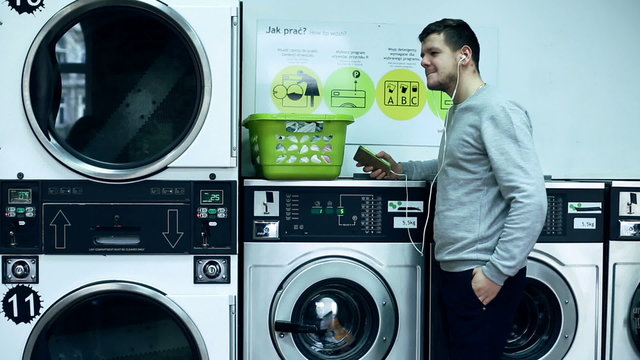 Young man listening to music on cellphone in public laundry
