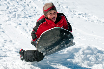 Fototapeta na wymiar Adorable boy riding sled down snow hill.