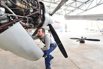 Flugzeugmechaniker repariert Turbine eines Flugzeuges im Hangar eines Flughafens // Aircraft mechanic repaired turbine of an airplane in an airport hangar - obrazy, fototapety, plakaty