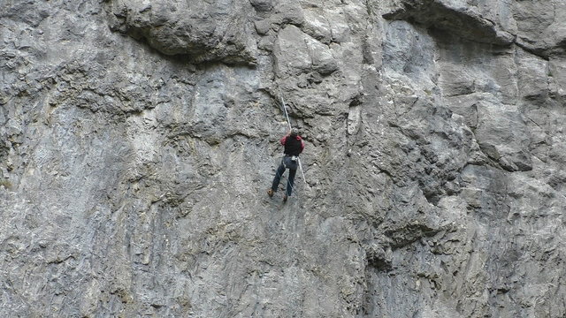 Mountaineer uses extendable pole to clip the rope into bolt hanger on vertical mountain wall