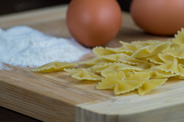 Farfalle fatte in casa con farina, uova, e mattarello su tagliere in legno su tavolo in legno antico