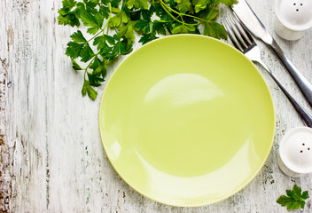 Empty green plate and fresh parsley on rustic white wooden background, place for text