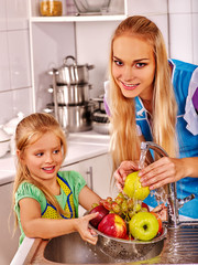 Mother and little ones kid is washing fruit at kitchen.