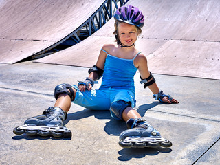 Girl wearing roller skates and helmet sitting on ride in skatepark.