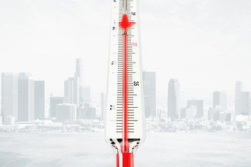 Thermometer with red mercury downward arrow at city background