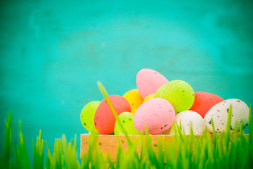 Basket of colorful Easter eggs in the grass on a blue background.