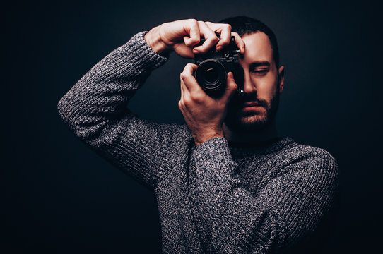 Young male photographer with beard taking pictures with retro camera