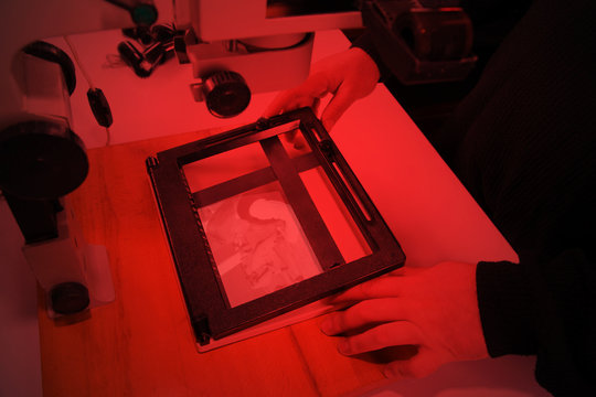 Photographer in the laboratory with  enlarger projects the image from a negative on photo paper