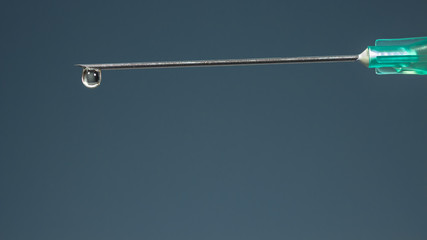 The tip of a hypodermic needle with a drop of drug, on dark blue background
