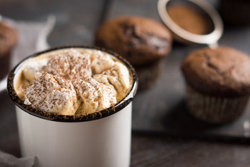 Cup of hot cocoa with marshmallows and chocolate muffins on the dark rustic wooden background