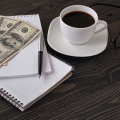 notebook with pen, cup of coffee, dollars and glasses