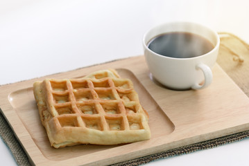 Waffle and hot coffee on wooden coaster.
