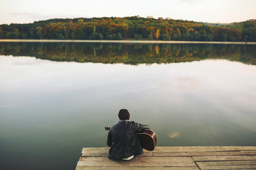 Fototapeta premium Young man playing on guitar at the lake