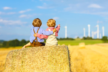 Two little twin boys and friends sitting on hay stack 