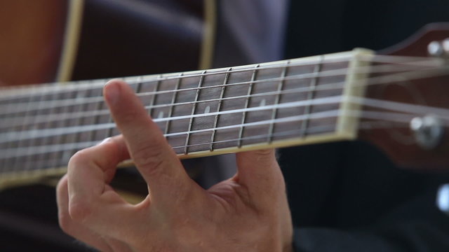 european man plays guitar chords on fingerboard