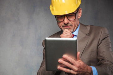 senior engineer wearing a helmet thinking and holding a tablet