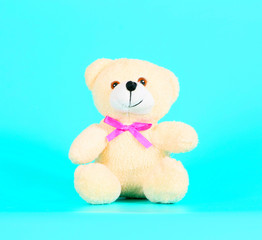 Cute teddy bear on a turquoise background. Soft toy in a pink bow. Toy close up.