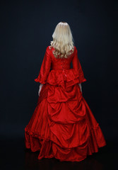 full length portrait of a beautiful blonde woman wearing a historical red silk, victorian era ball gown.