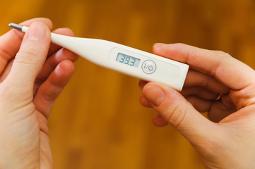 hands hold thermometer with high temperature on screen