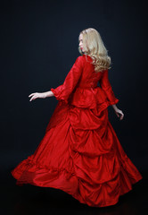 full length portrait of a beautiful blonde woman wearing a historical red silk, victorian era ball gown.