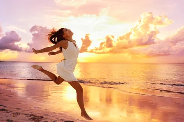 Foto op Canvas Freedom wellness well-being happiness concept. Happy carefree Asian woman feeling blissful jumping of joy on peaceful beach at sunset. Serenity, relaxation, mindfulness, stress free concepts. © Maridav