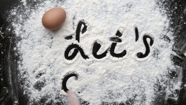 Female baker hand writing on the back board with flour and egg. Concept of food preparation and bakery. 