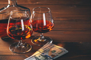 Two glasses of cognac and bottle, with wad of money on the wooden table.
