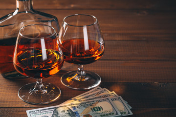 Two glasses of cognac and bottle, with wad of money on the wooden table.