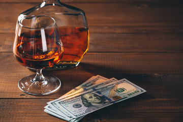 Glass with cognac and bottle, with wad of money on the wooden table.
