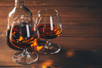 Two glasses of cognac and bottle on the wooden table.