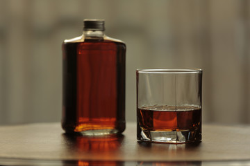 Bottle and glass with whisky together on leather and mahogany table