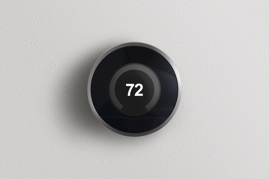 A simplistic photo of a round, modern, programmable digital thermostat, on a clean white wall.