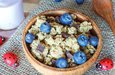 Crunchy musli with blueberries, kiwi and yogurt in wooden bowl on table set 