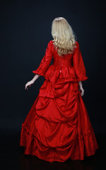 full length portrait of a beautiful blonde woman wearing a historical red silk, victorian era ball gown.