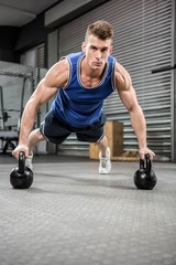 Obraz na płótnie Canvas Muscular man doing push up with kettlebells