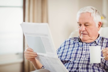 Fototapeta premium Senior man reading newspaper in living room
