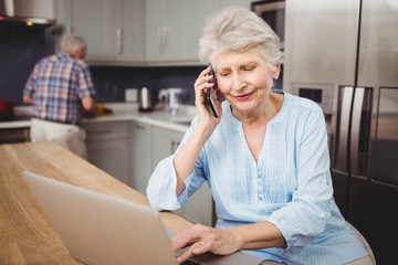 Senior woman talking on phone while using laptop and man working