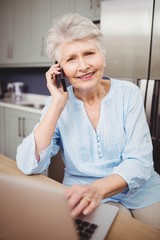 Senior woman talking on phone and using laptop